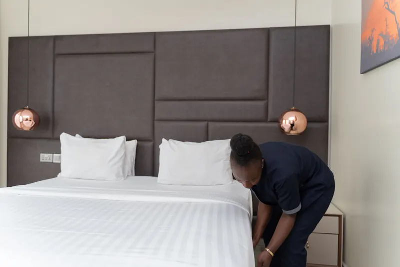 Zimmermädchen macht ein weißes Bett in einem modernen Hotelzimmer